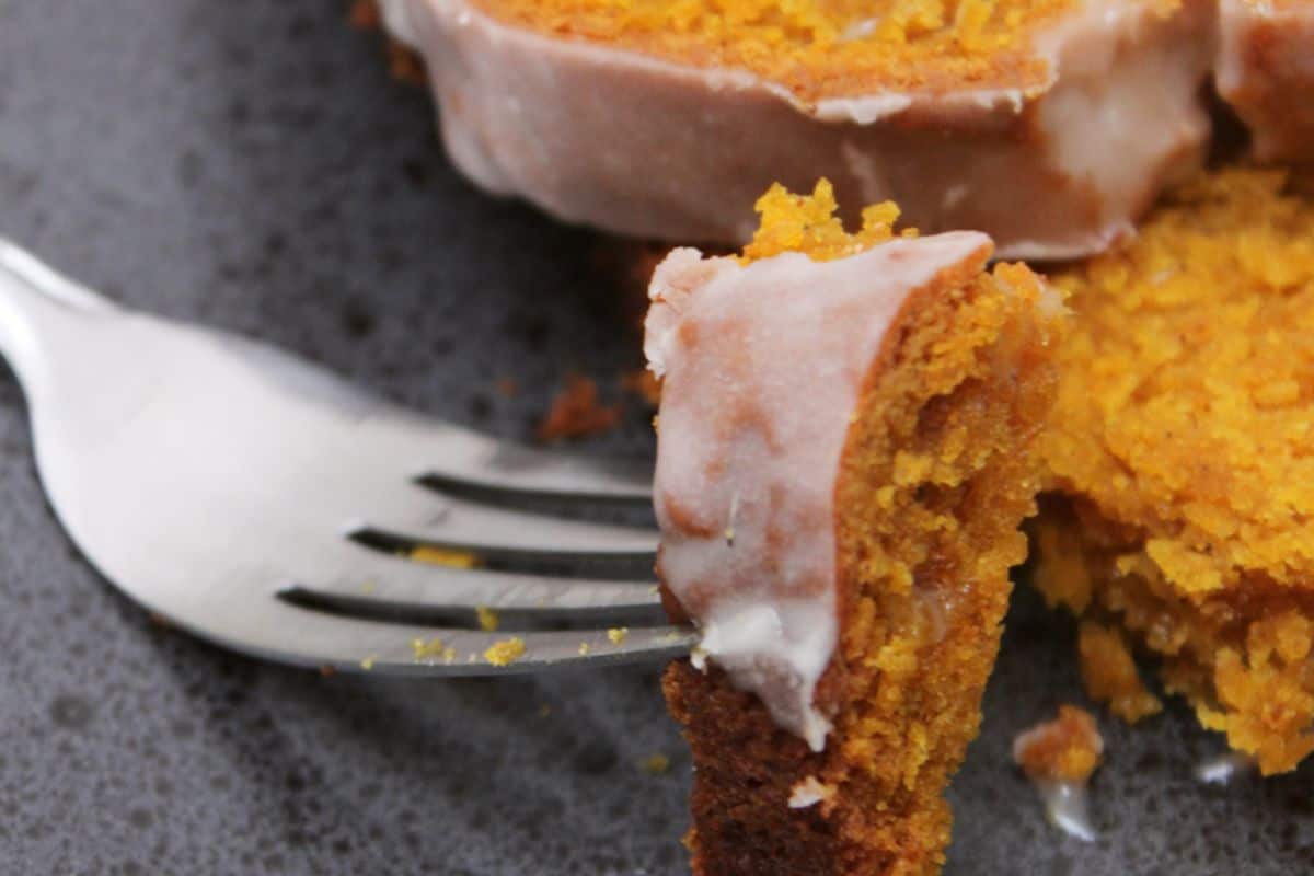 A fork holds a piece of pumpkin loaf with icing on a gray plate.