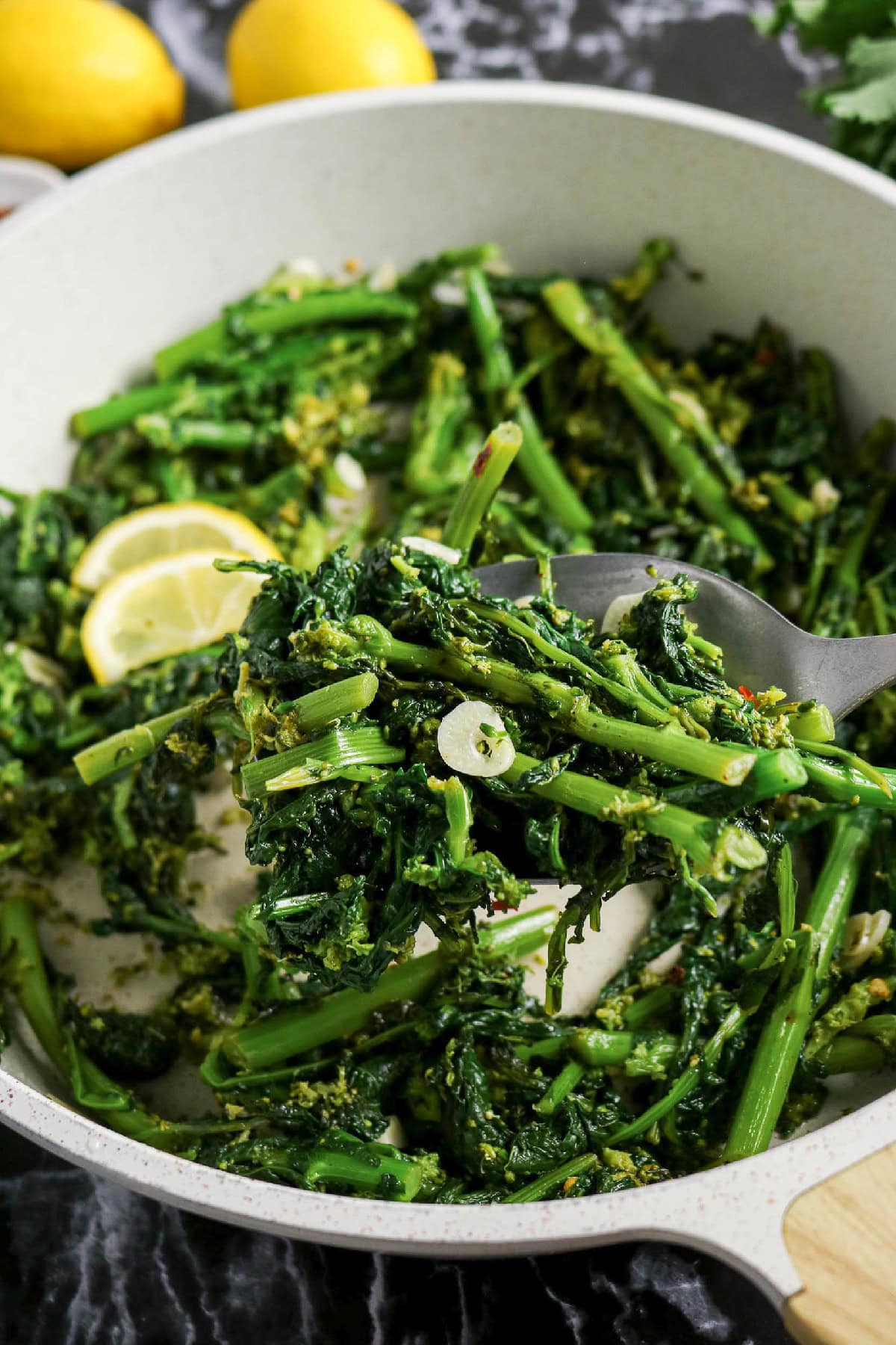 Spoonful of sautéed rapini with garlic and lemon in a skillet.