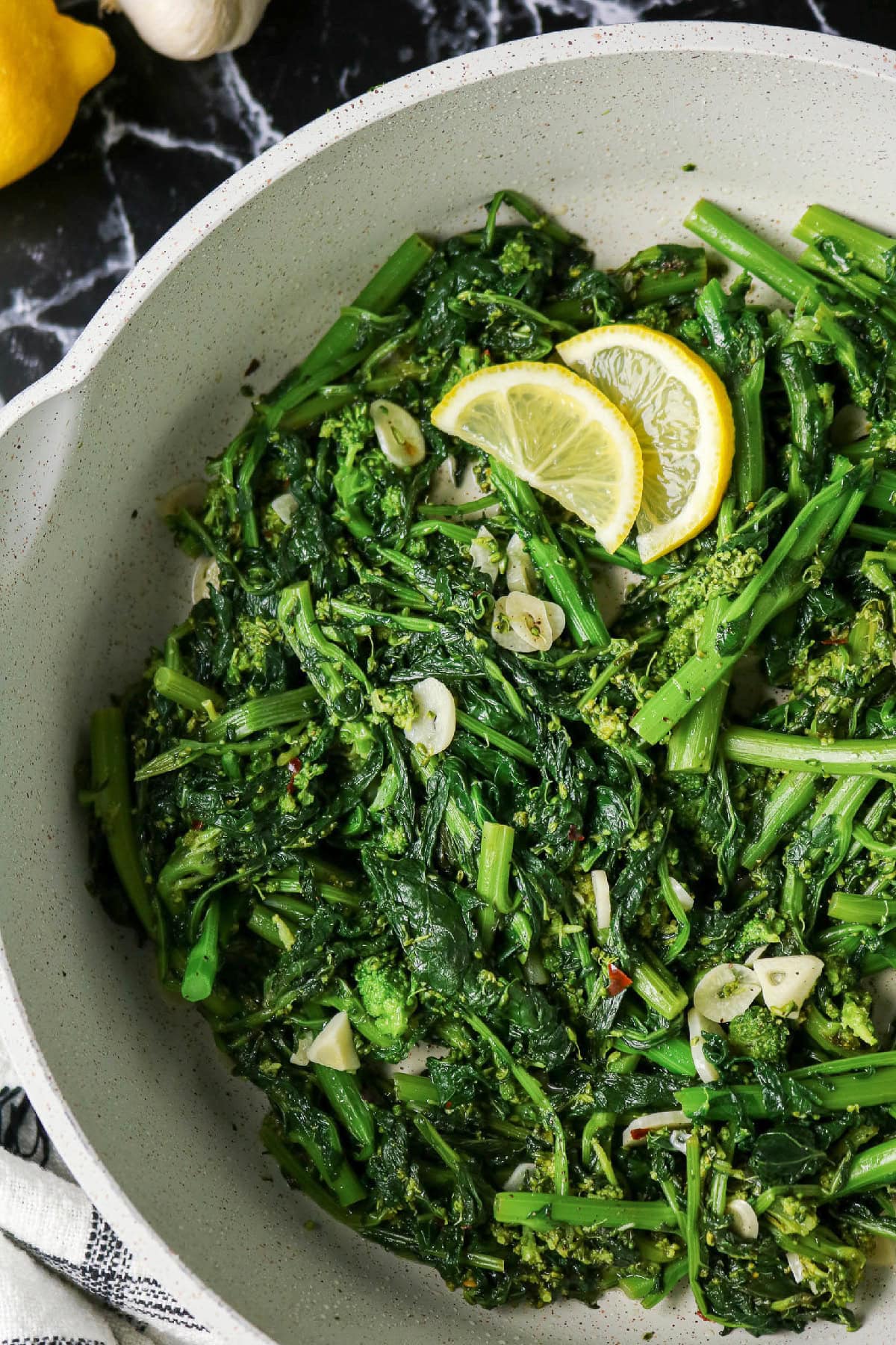 Close-up of sautéed rapini with sliced garlic and fresh lemon wedges.