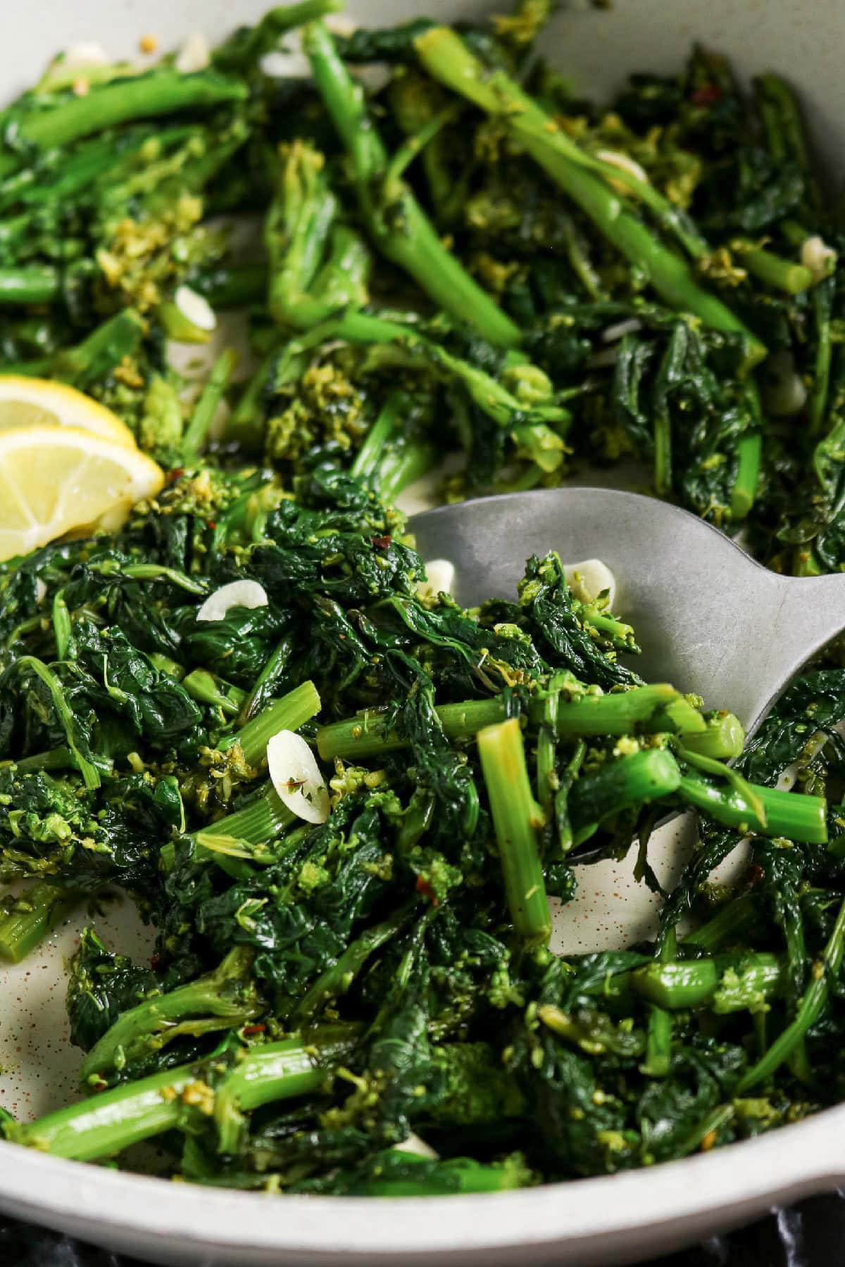 Close-up of sautéed rapini with sliced garlic being lifted with a spoon.
