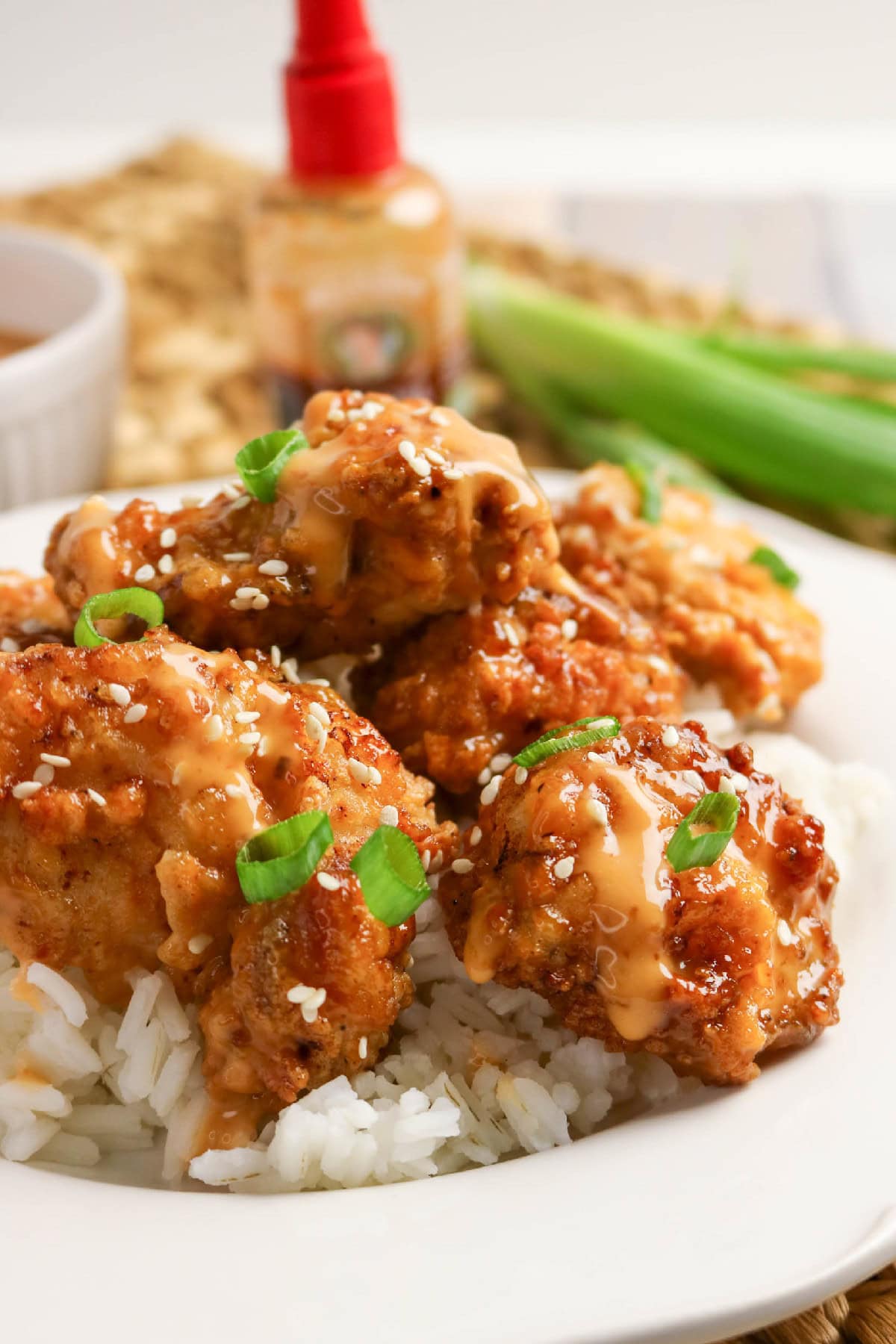 Close-up of saucy bang bang chicken served over white rice with green onions and sesame seeds.