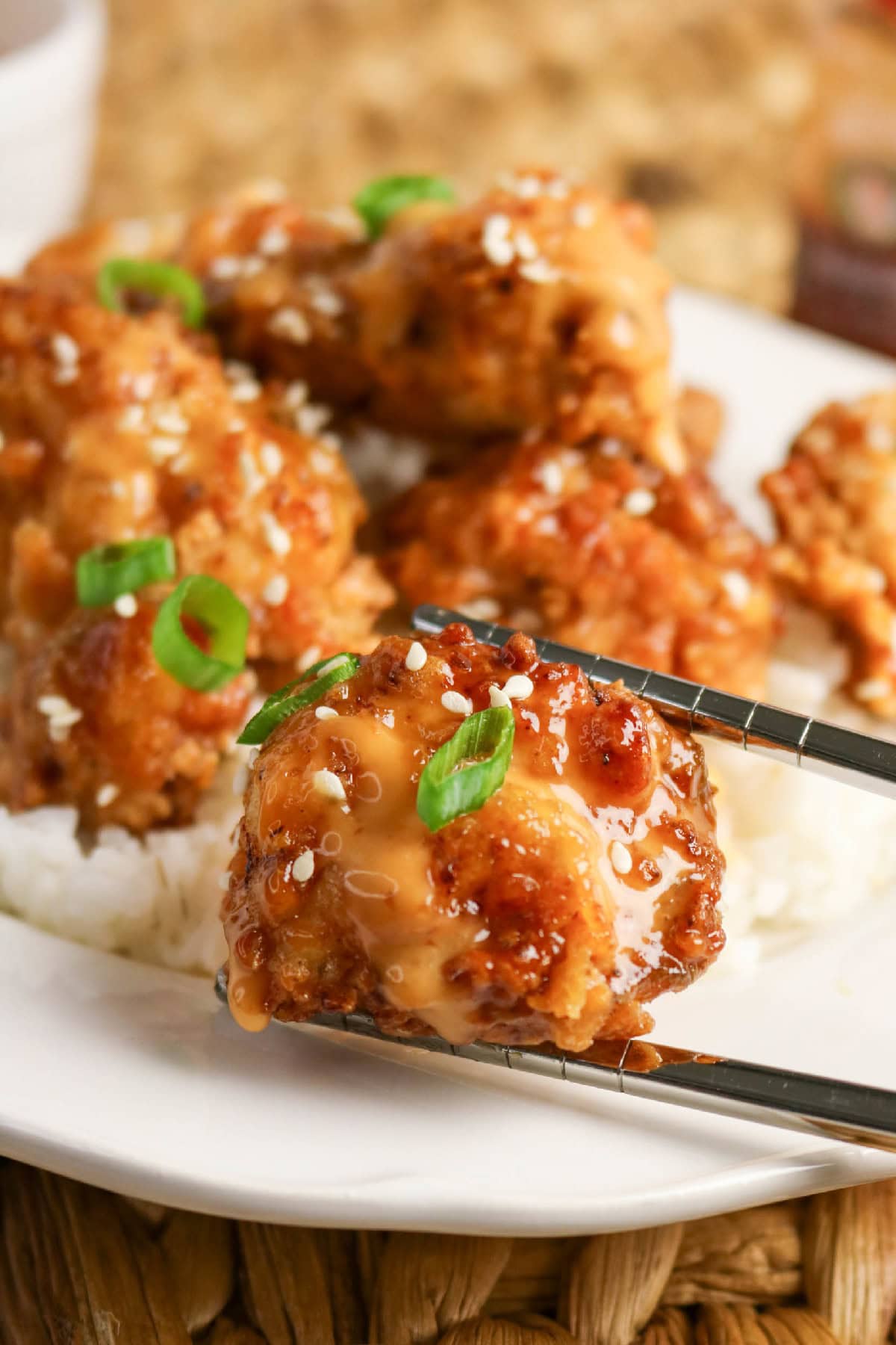 A piece of bang bang chicken held with chopsticks over a plate of rice.