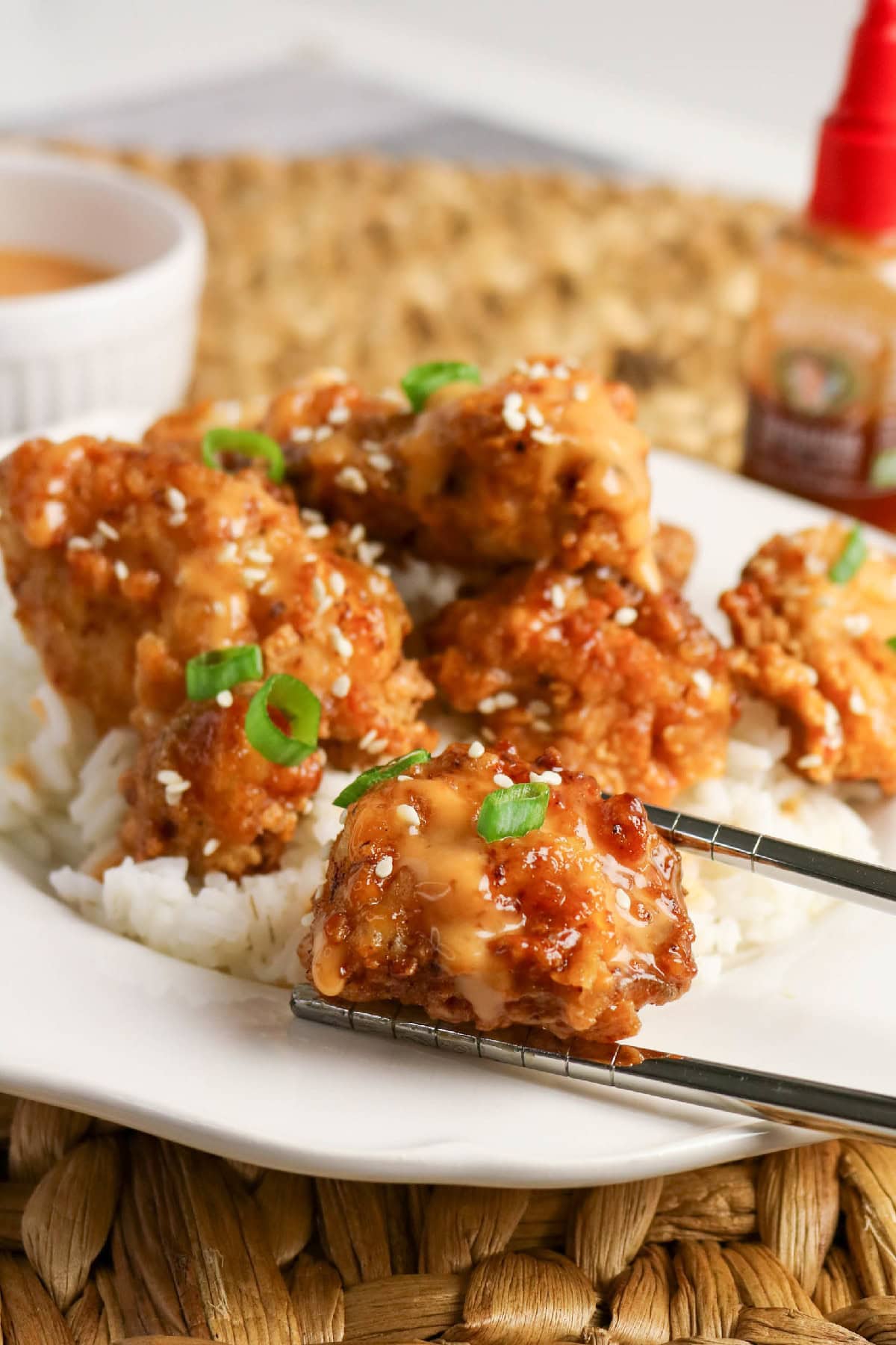Chopsticks holding a saucy piece of bang bang chicken over white rice.