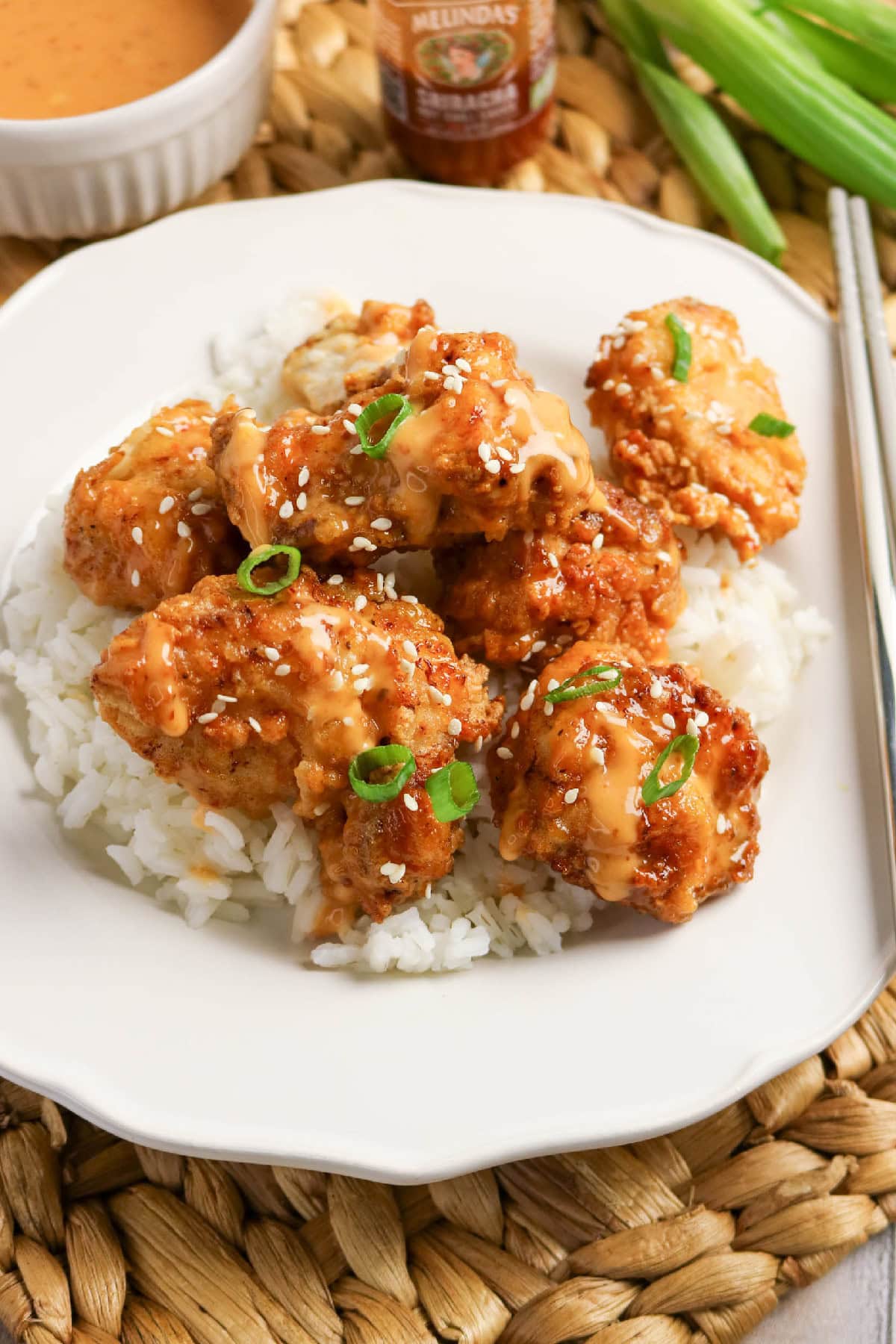 Plate of bang bang chicken served over white rice with extra sauce and green onions.