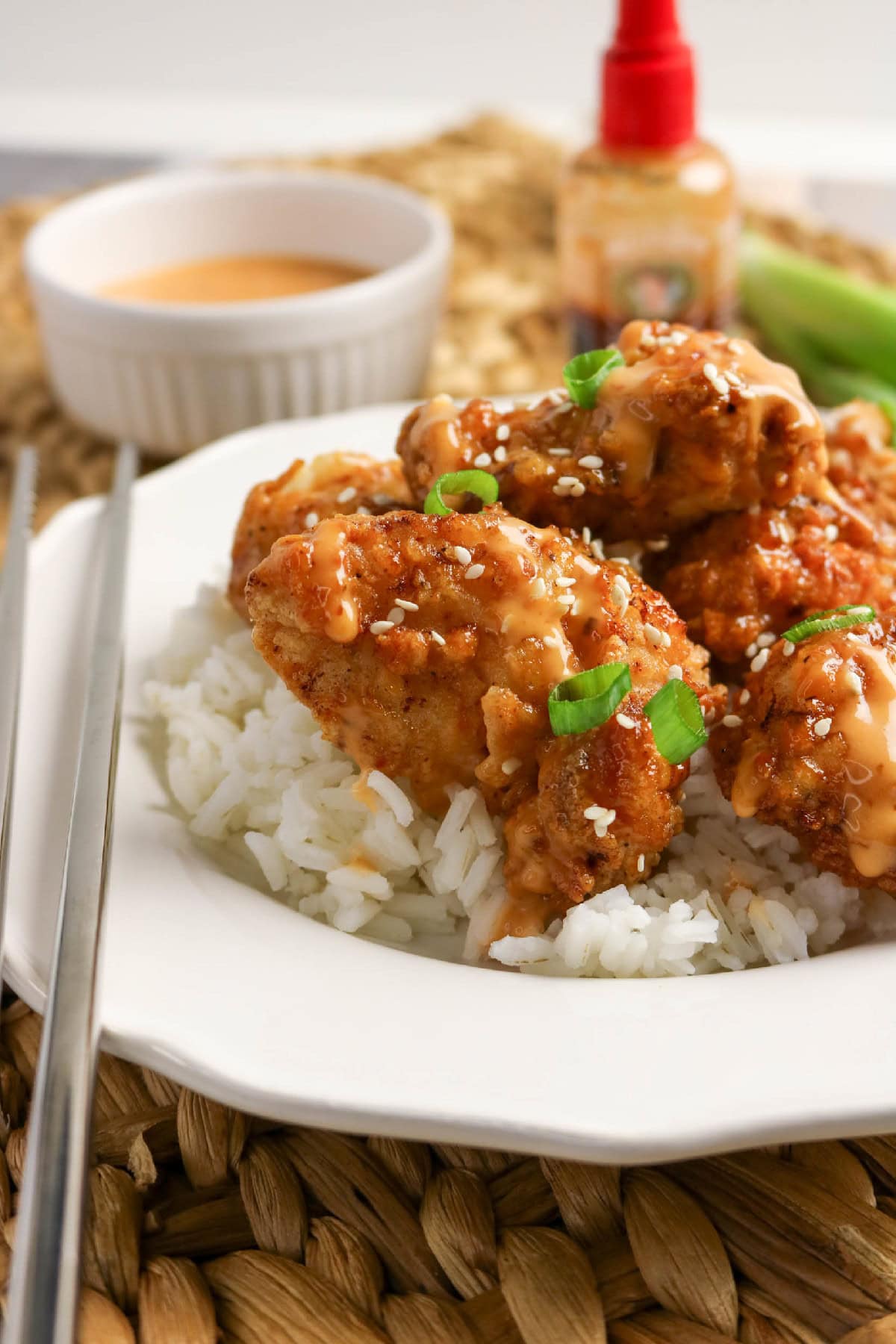 Close-up of crispy bang bang chicken with creamy sauce, sesame seeds, and sliced green onions.