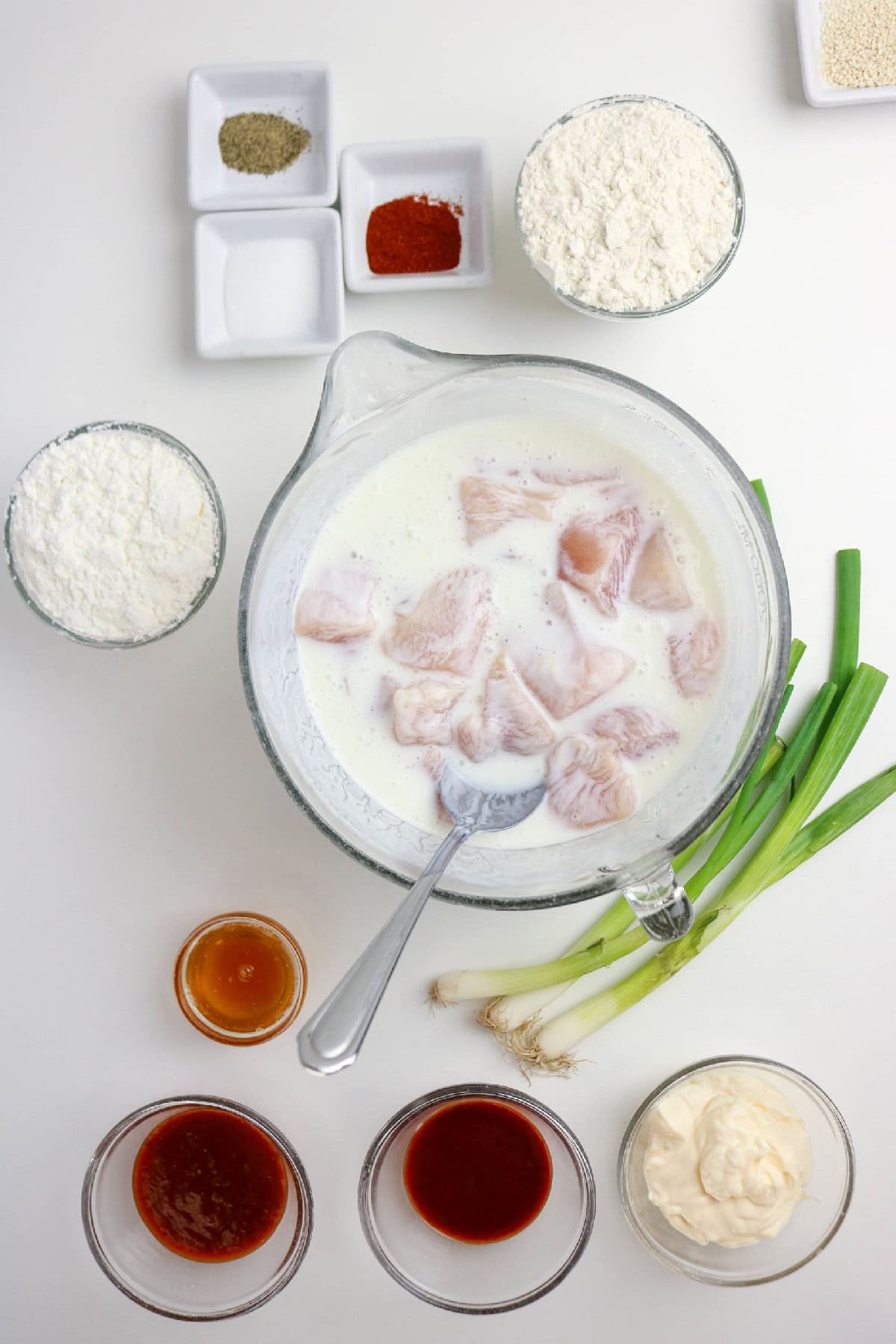 Chicken pieces soaking in buttermilk in a glass bowl.