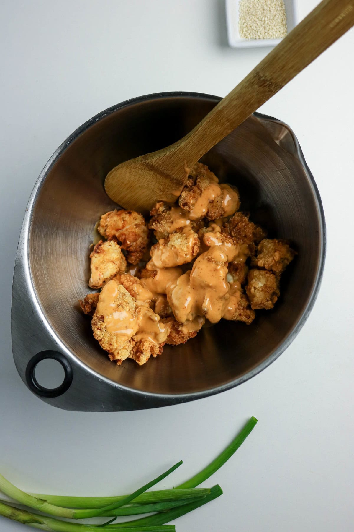 Fried chicken pieces being tossed with creamy bang bang sauce.