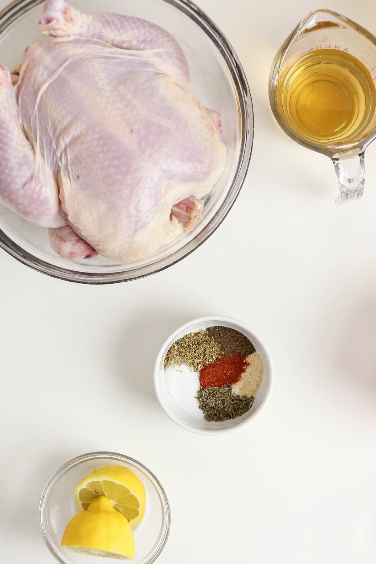 Whole raw chicken with broth, seasonings, and lemon arranged for chicken and orzo soup.