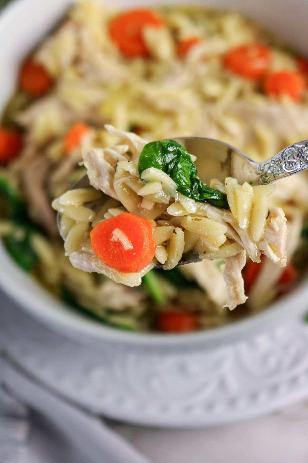 Close-up chicken and orzo soup with carrots and spinach.