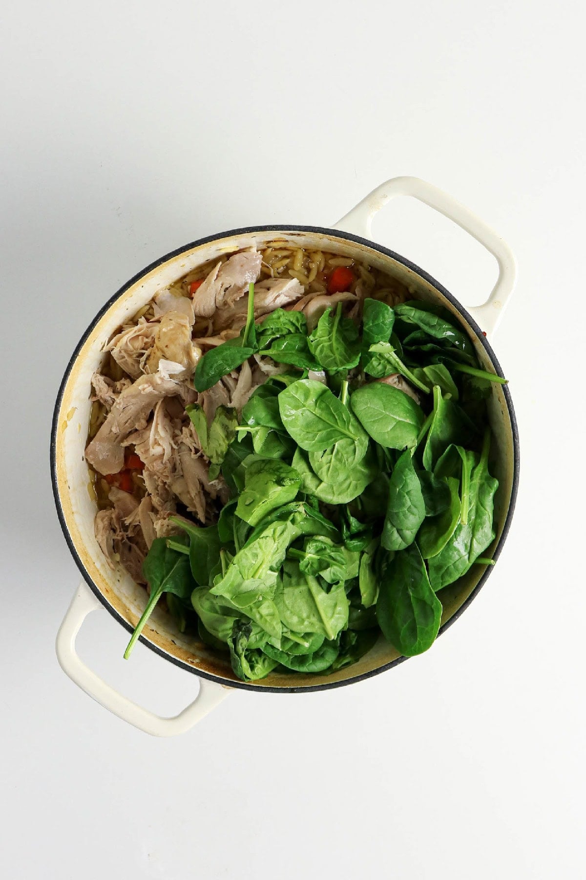 Chicken and orzo soup with shredded chicken, carrots, celery, and spinach in a Dutch oven.