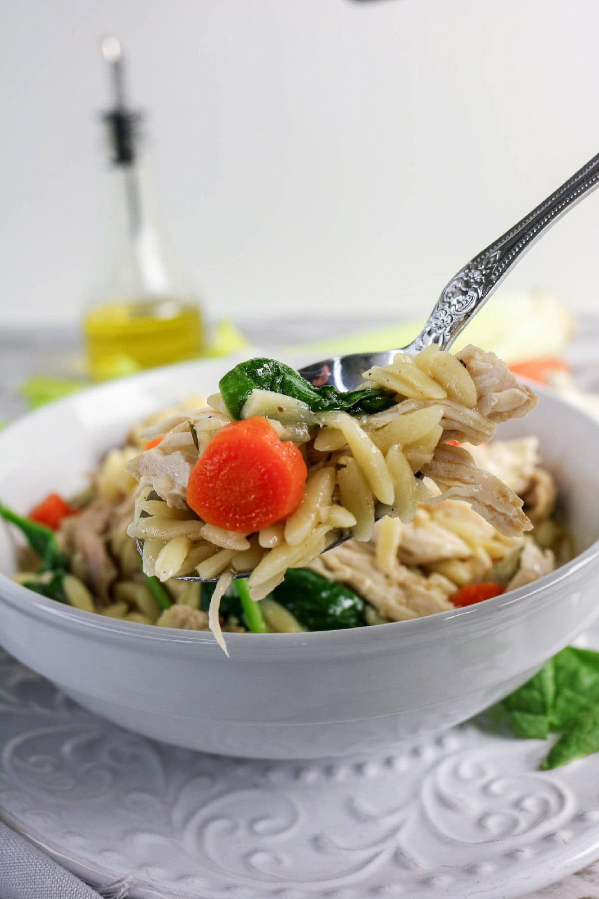 Spoon lifting chicken, orzo, spinach, and carrots from soup.