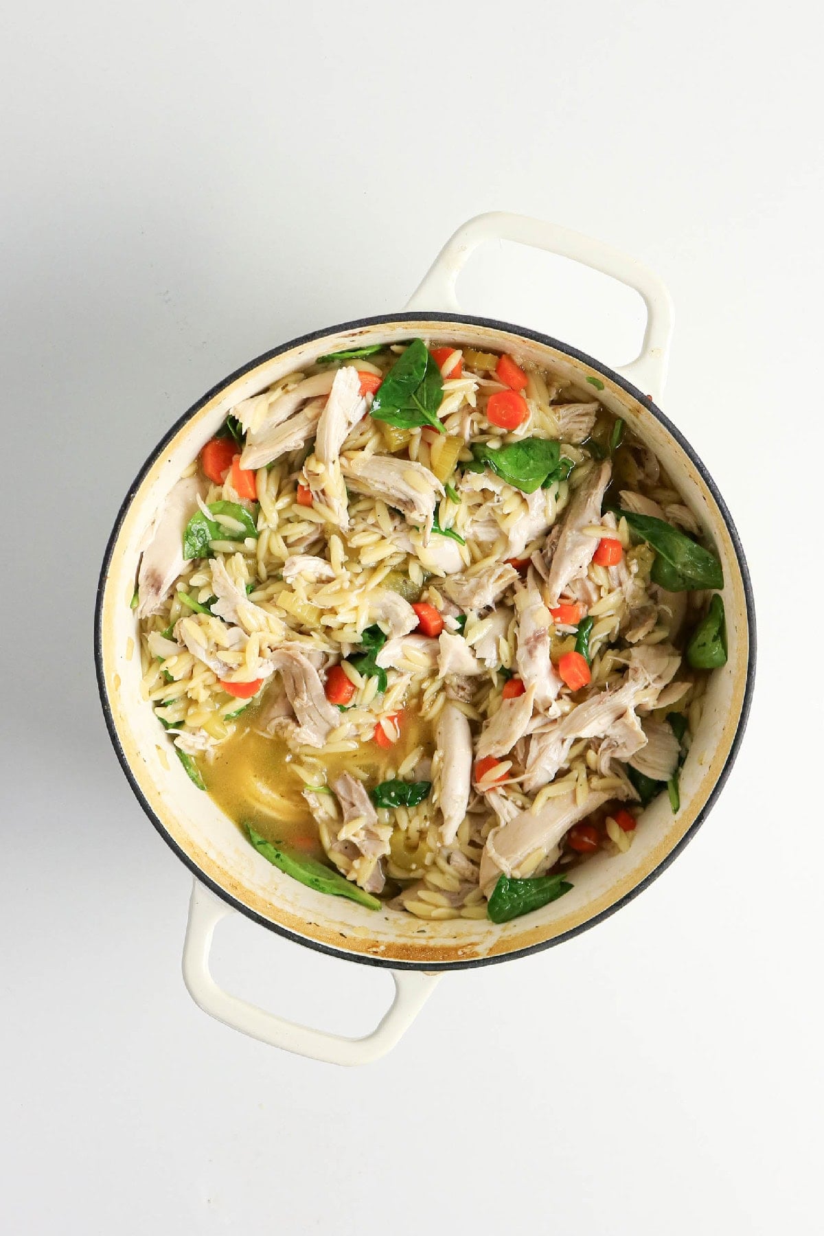 Close-up of chicken and orzo soup with shredded chicken, carrots, celery, and spinach.