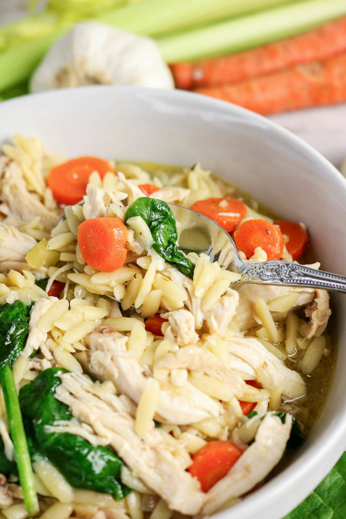 Close-up chicken and orzo soup with carrots and spinach.