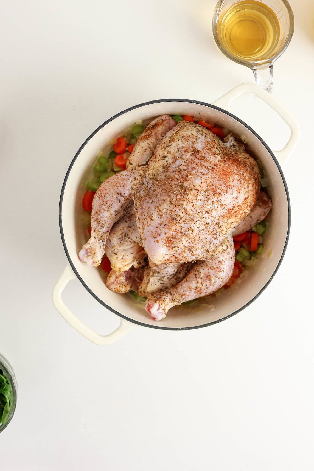 Seasoned whole chicken placed over sautéed vegetables in a Dutch oven.