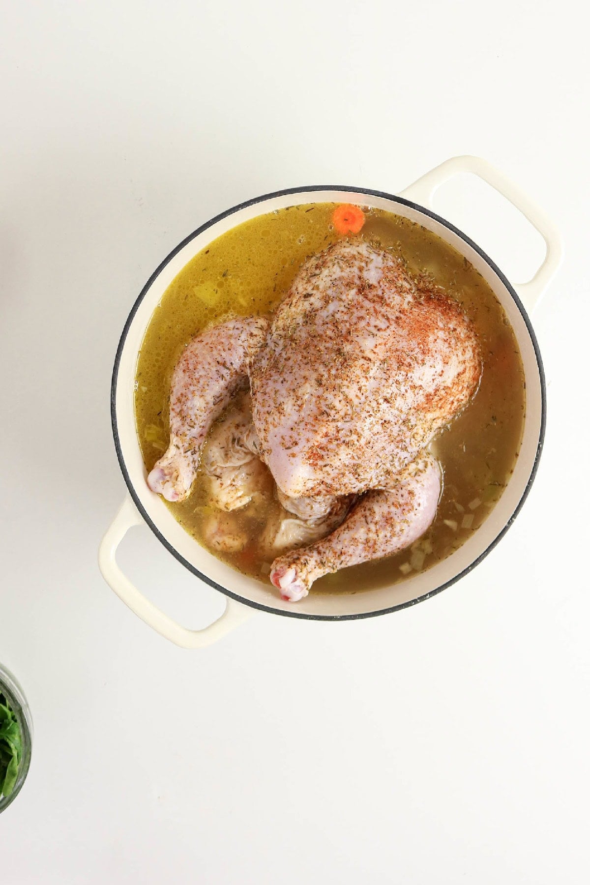 Seasoned whole chicken simmering in broth with vegetables.