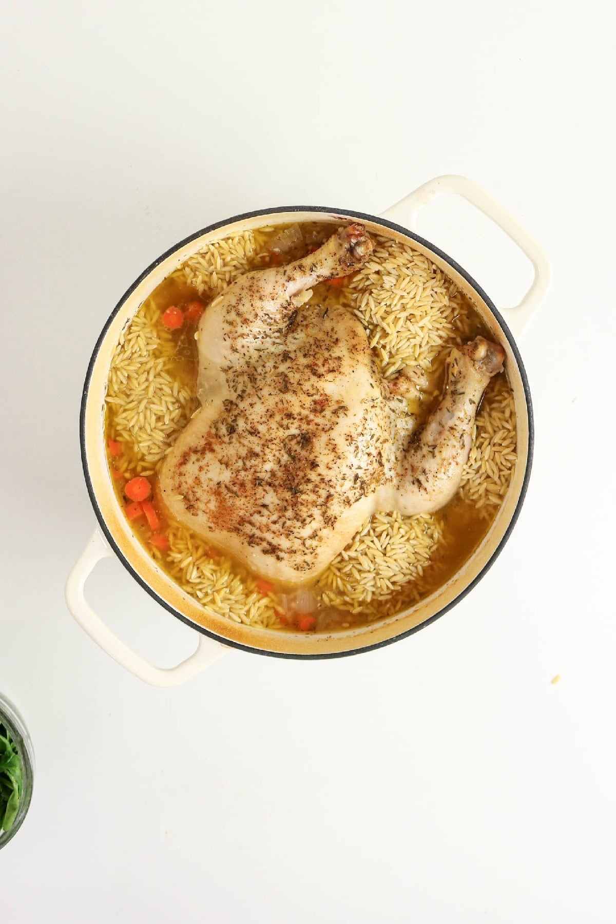 Cooked whole chicken with orzo, carrots, and broth in a Dutch oven.