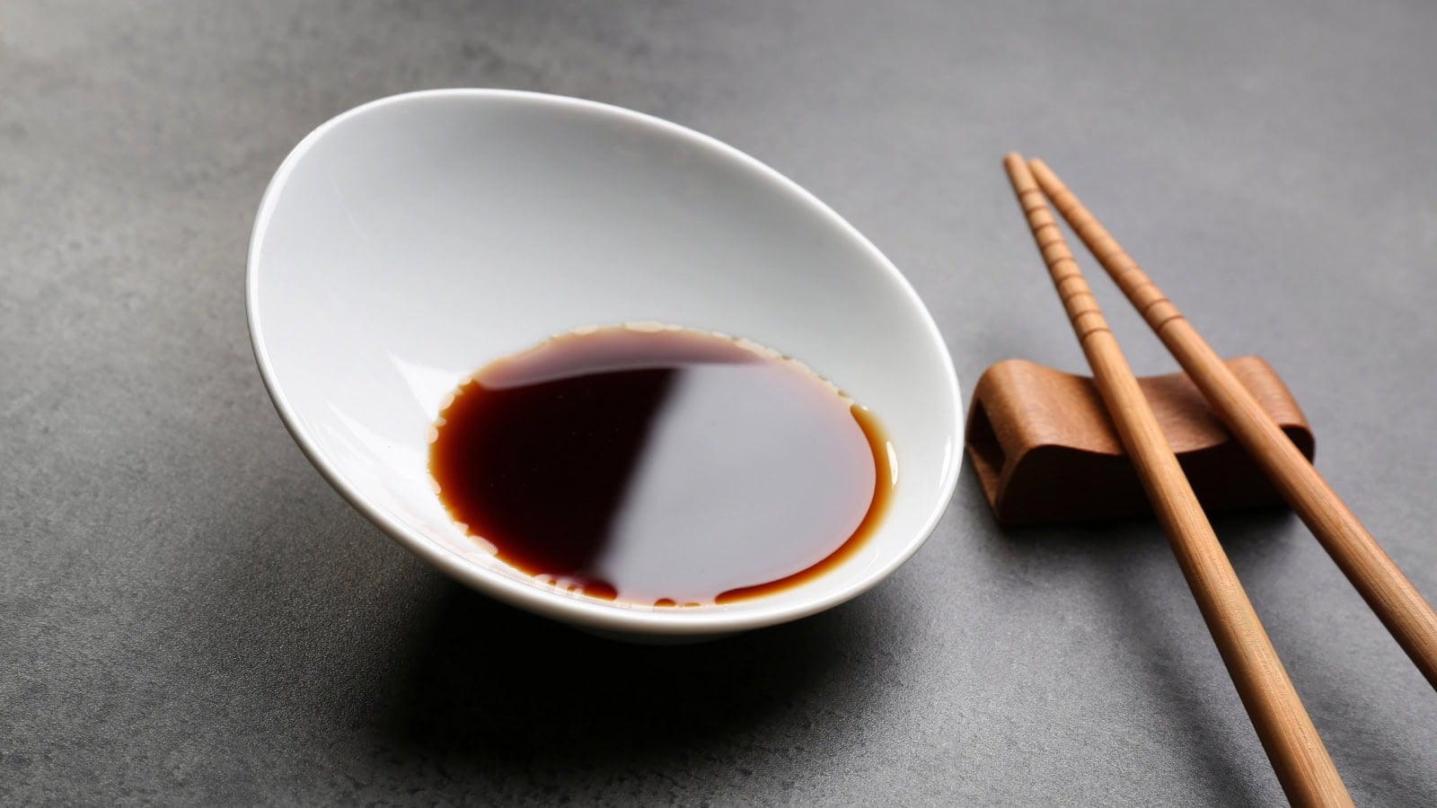 White bowl of soy sauce with chopsticks on a gray surface.