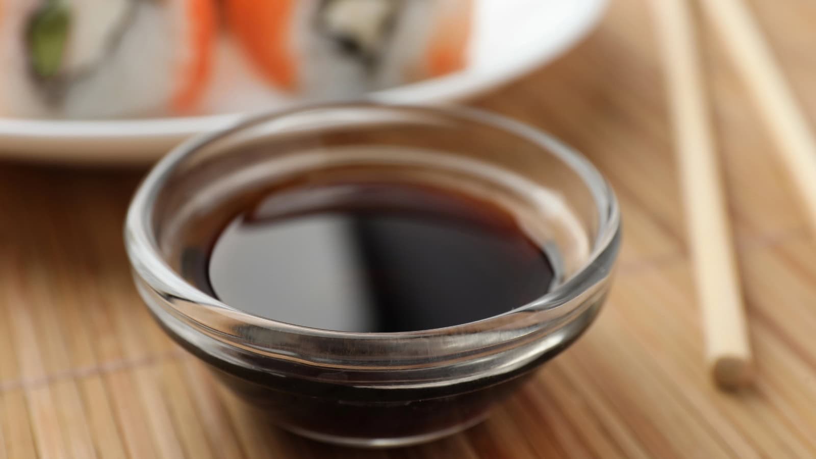 Bowl of dark soy sauce with sushi in the background.