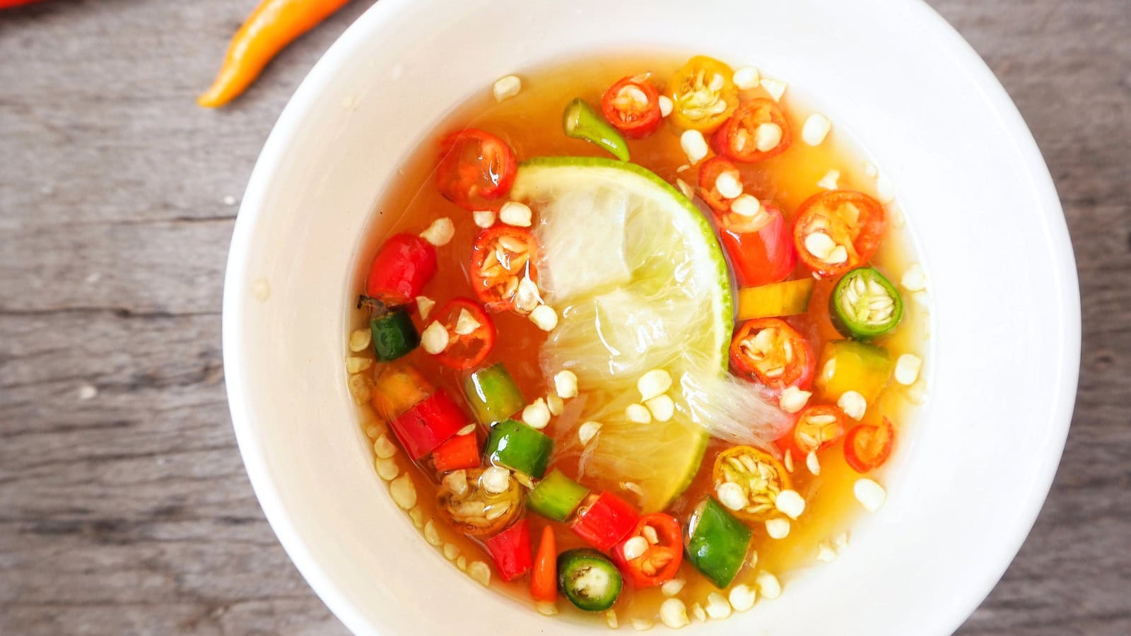 Bowl of fish sauce with sliced red and green chilies and lime.