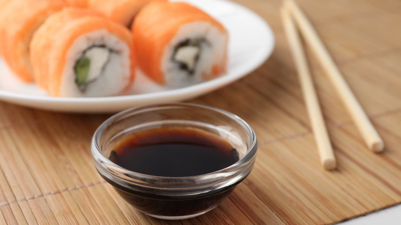 Bowl of soy sauce with sushi rolls and chopsticks.