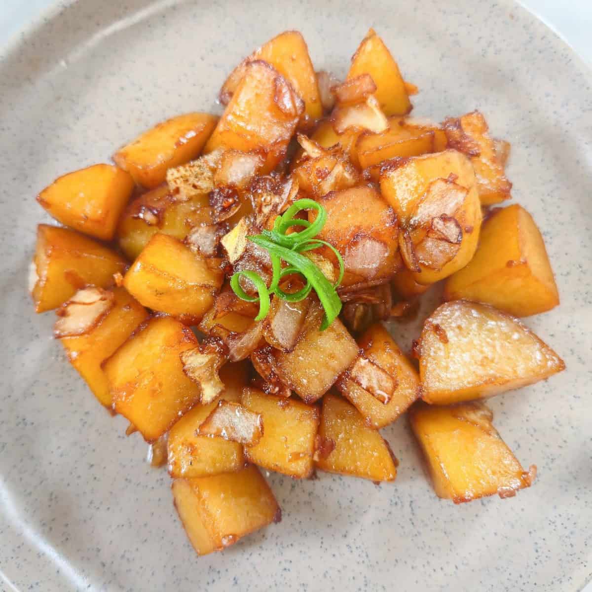 Glazed potatoes with caramelized onions and scallion strips served on a plate.