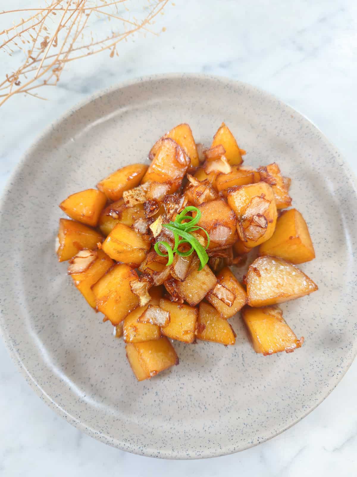 Glazed potatoes with caramelized onions and scallion strips served on a ceramic plate.
