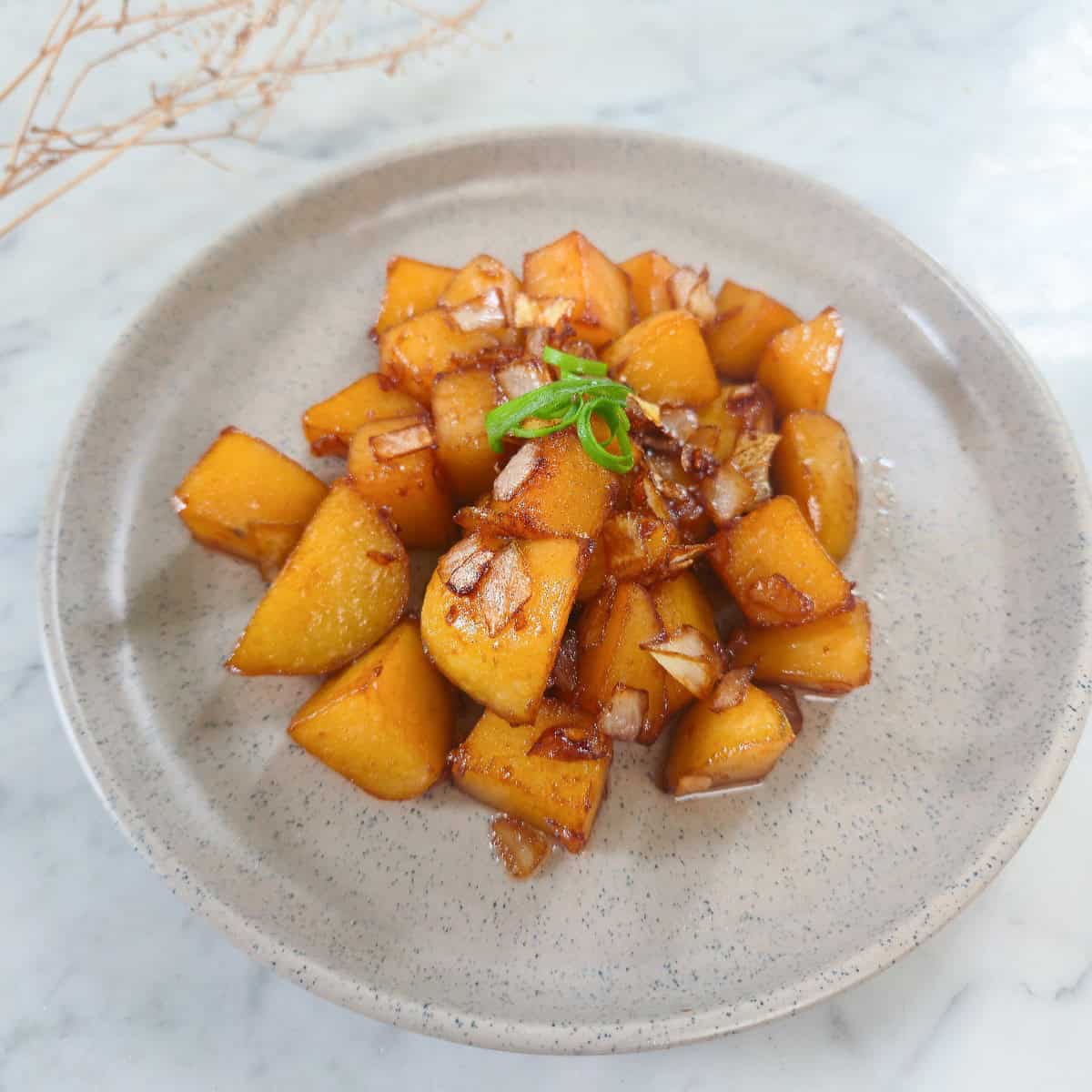 Golden glazed potatoes with caramelized onions and green scallion garnish on a ceramic plate.