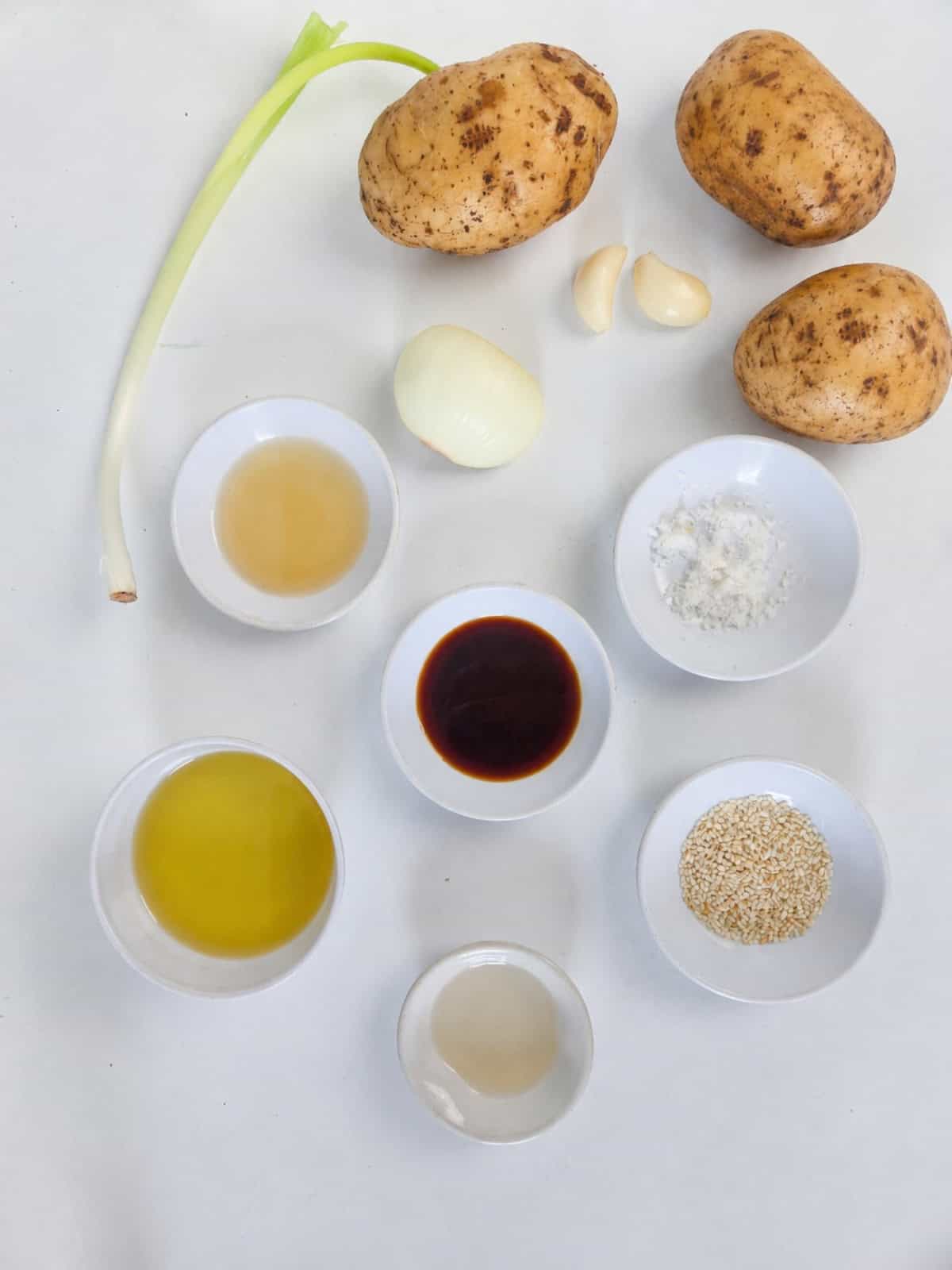 Ingredients for glazed potatoes including potatoes, scallion, onion, garlic, soy sauce, mirin, cooking oil, sesame oil, salt, and sesame seeds.