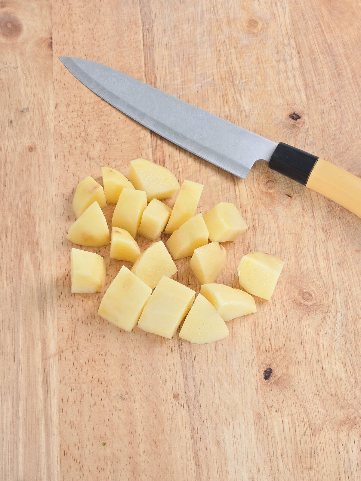 Peeled potatoes cut into medium-sized chunks on a wooden cutting board with a kitchen knife.