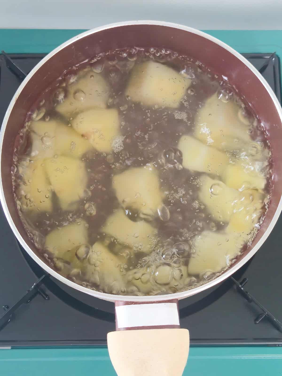 Potato chunks boiling in a pot of water until partially tender.