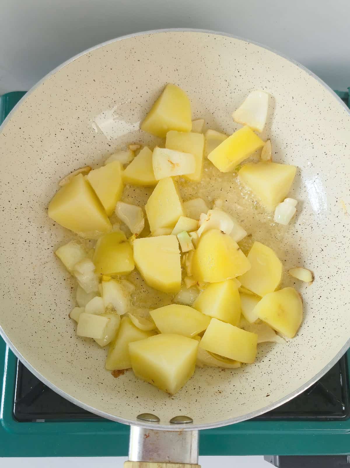 Boiled potato chunks cooking with onion and garlic in a skillet.