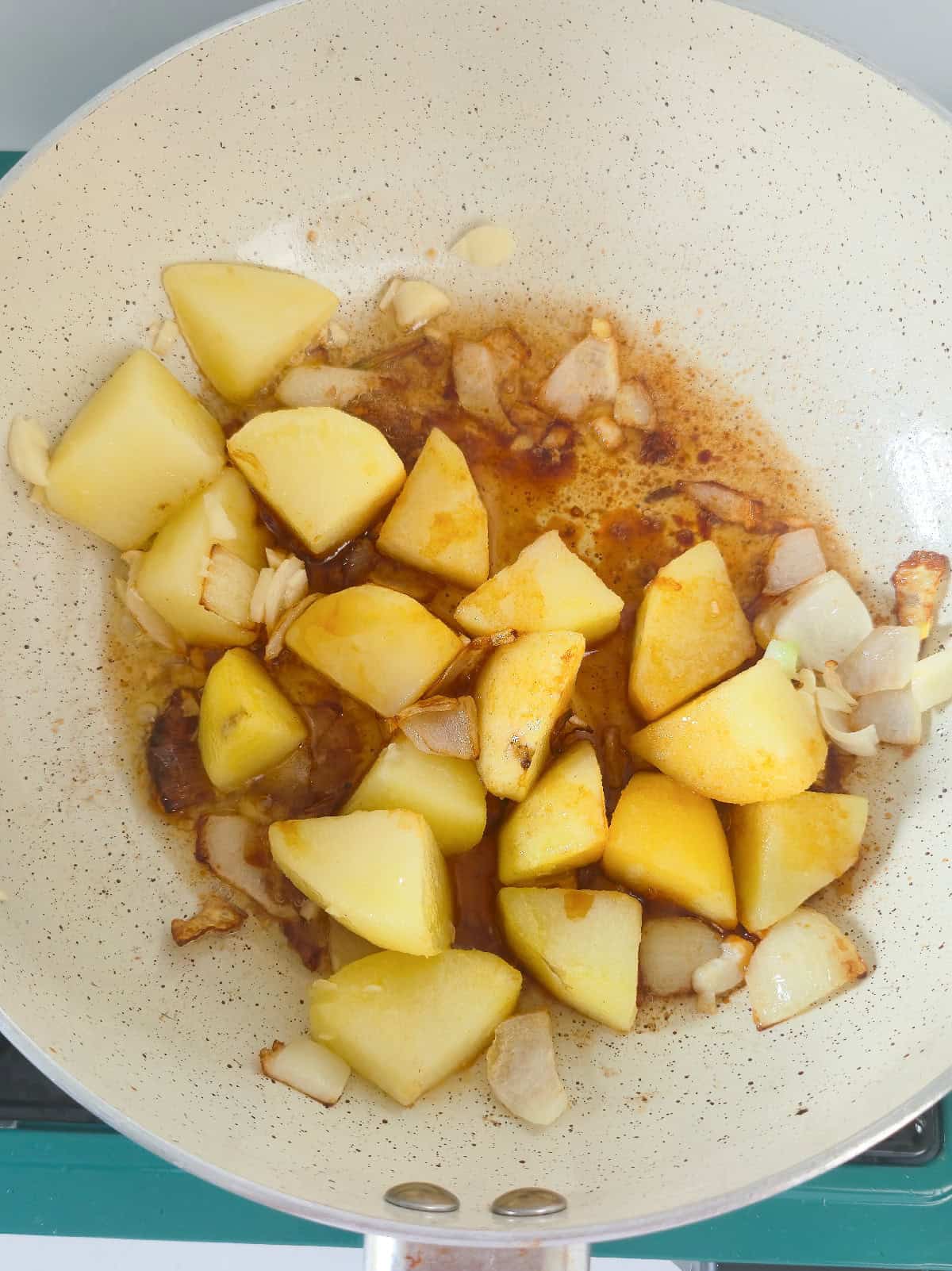 Potato chunks cooking with onion, garlic, and sauce in a skillet.