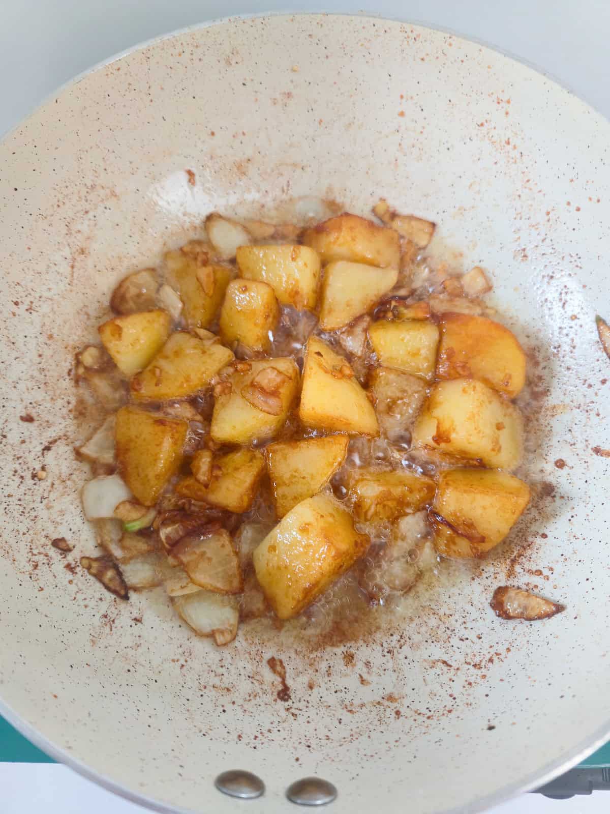Glazed potatoes simmering with onions in a savory sauce until golden and glossy.