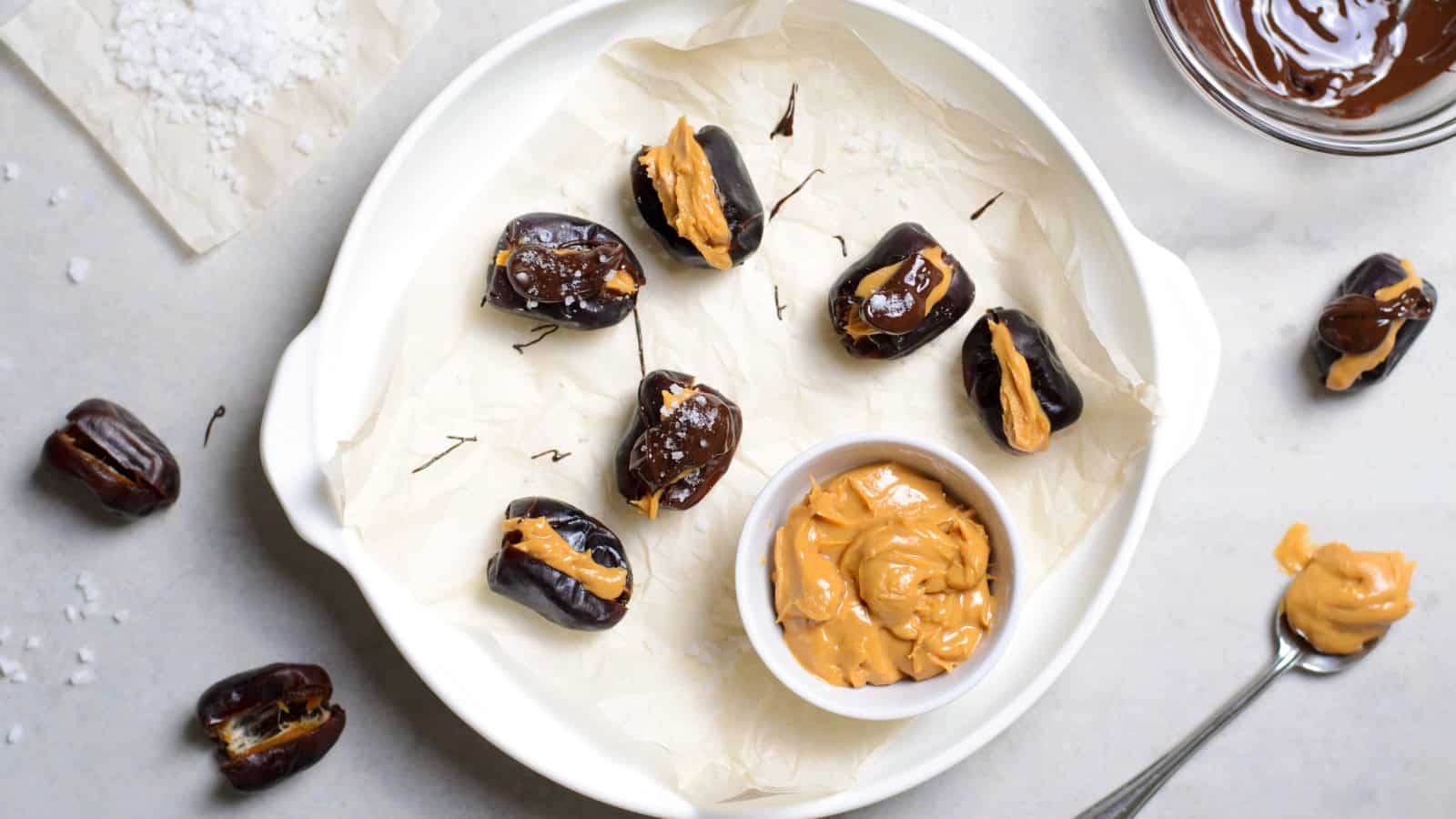 Dates stuffed with peanut butter on a plate, with melted chocolate and extra peanut butter nearby.