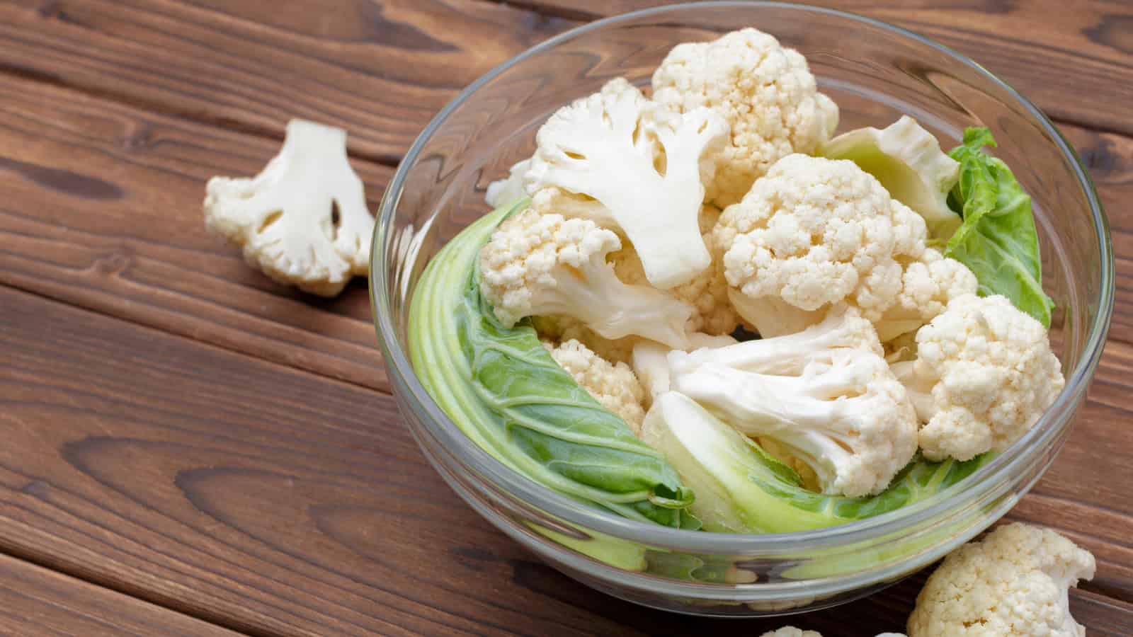 Fresh cauliflower florets in a glass bowl with leaves.