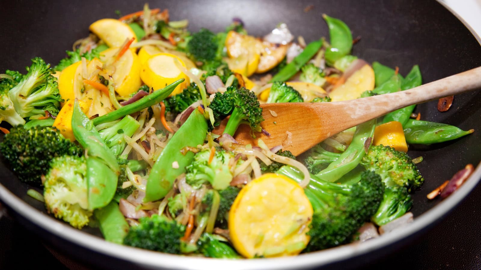 Stir-fried broccoli, snap peas, squash, and mixed vegetables in a wok.