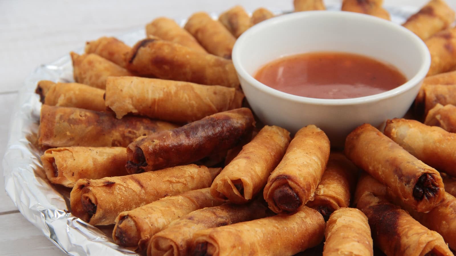 Crispy lumpia rolls with dipping sauce on a plate.