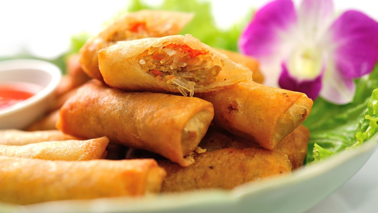 Crispy lumpia stacked on a plate with dipping sauce and lettuce.