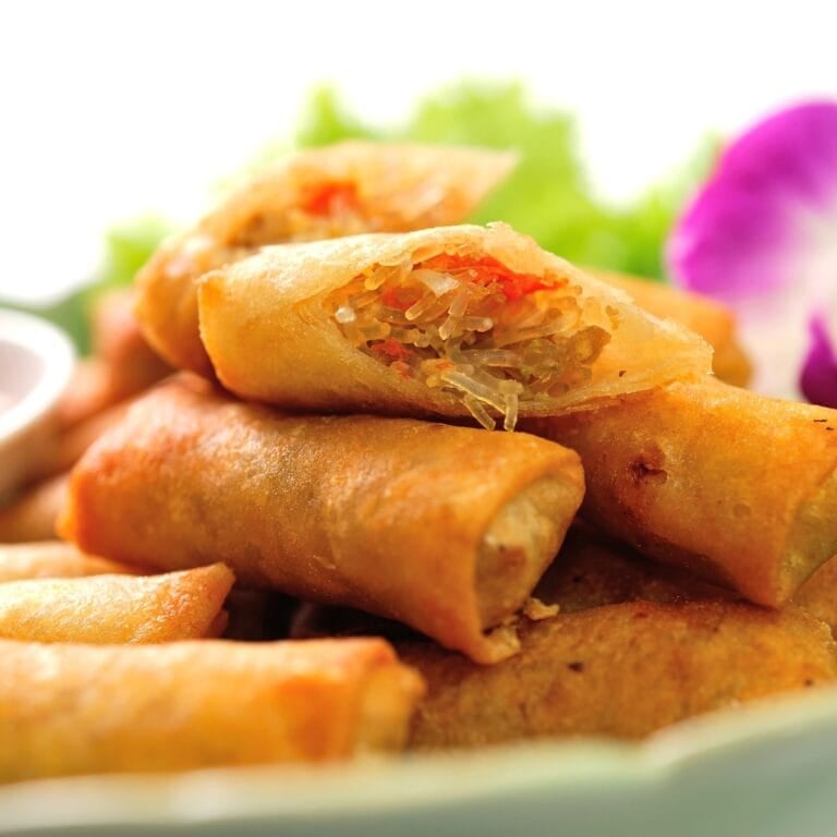 Crispy lumpia arranged on a plate, served with dipping sauce and fresh lettuce.