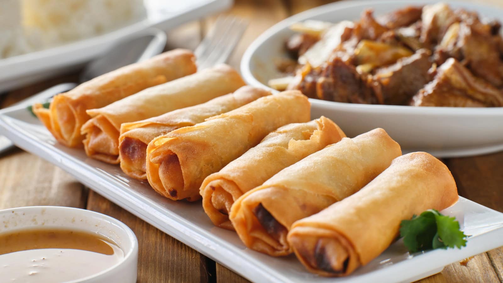 Crispy lumpia rolls served on a plate with dipping sauce.