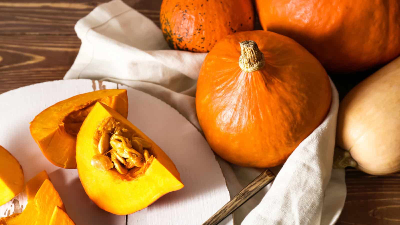 Whole and sliced pumpkins displayed on a wooden table with pumpkin seeds.