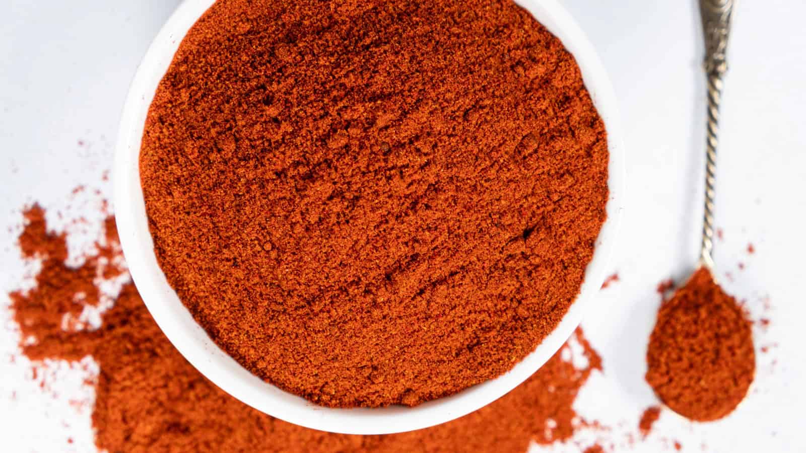 Bowl of red plant-based seasoning powder with a spoon and spilled seasoning.