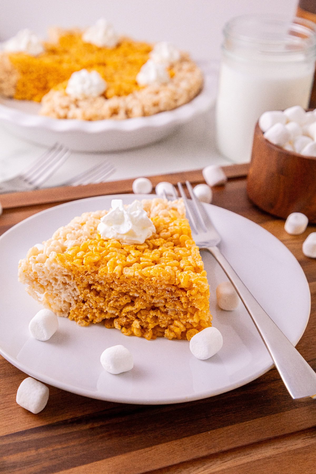 Pumpkin spice Rice Krispie treat pie slice served with marshmallows and a glass of milk.