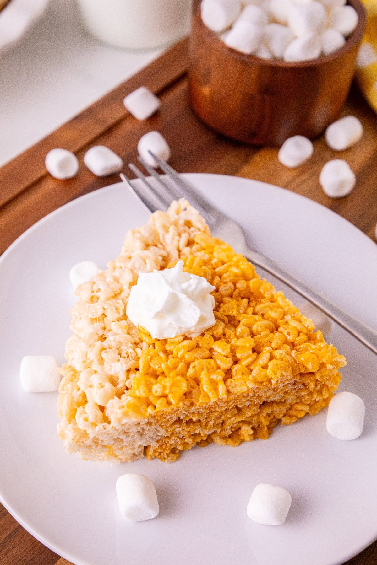 Close-up of a thick pumpkin spice Rice Krispie treat slice topped with whipped cream.