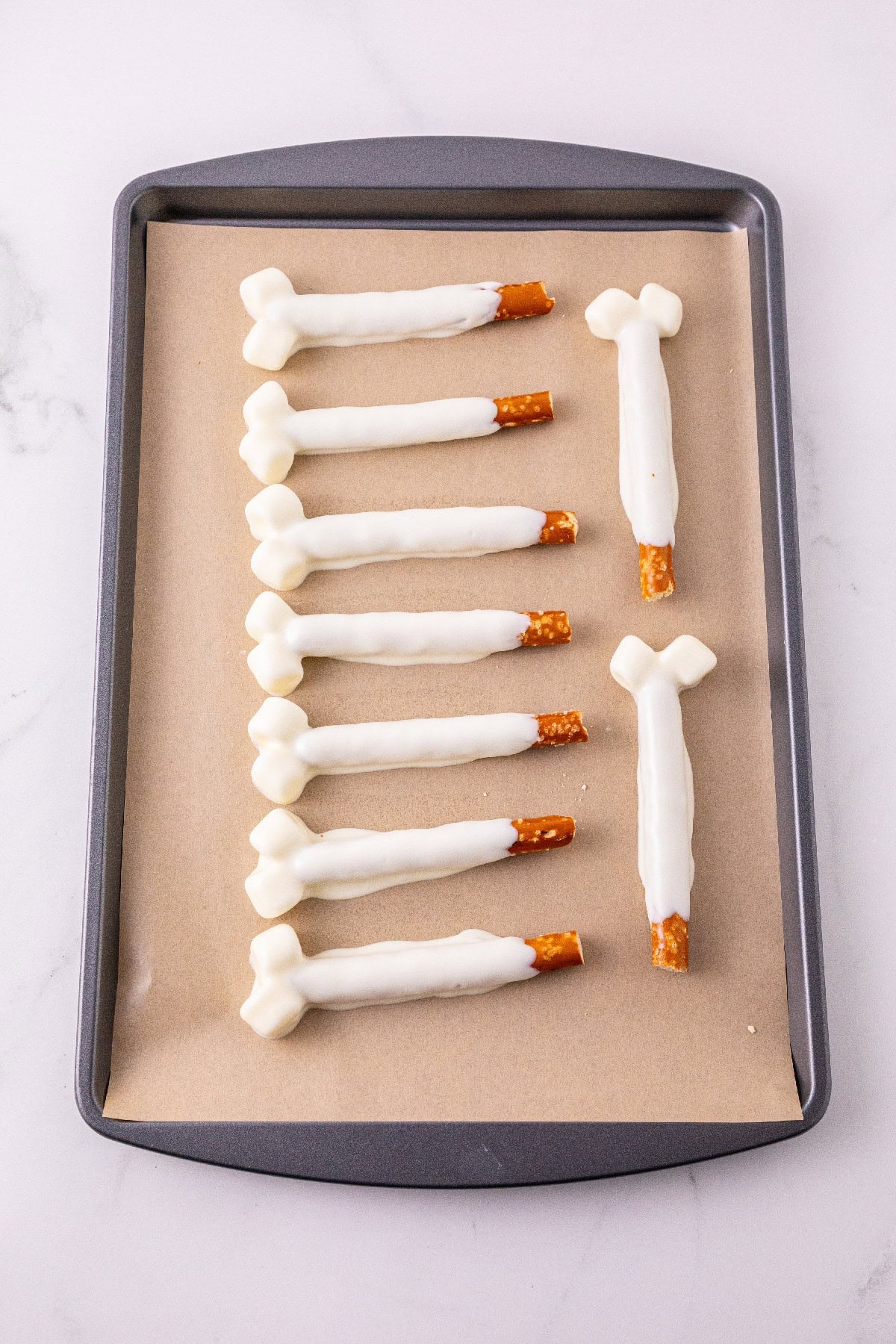 Finished white chocolate pretzel bones setting on a lined baking sheet.