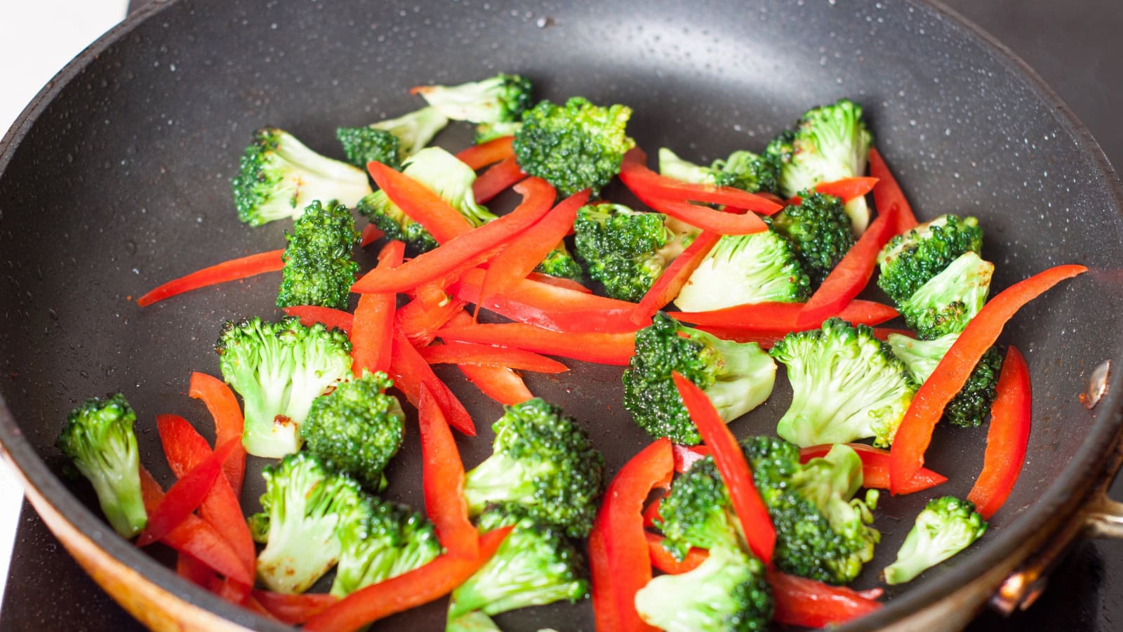 Broccoli and sliced red peppers sautéing in a pan.