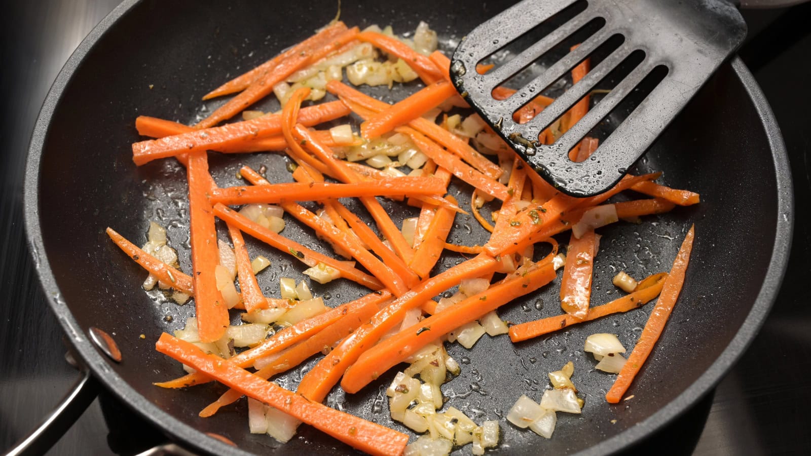 Carrots and onions sautéing in a skillet.