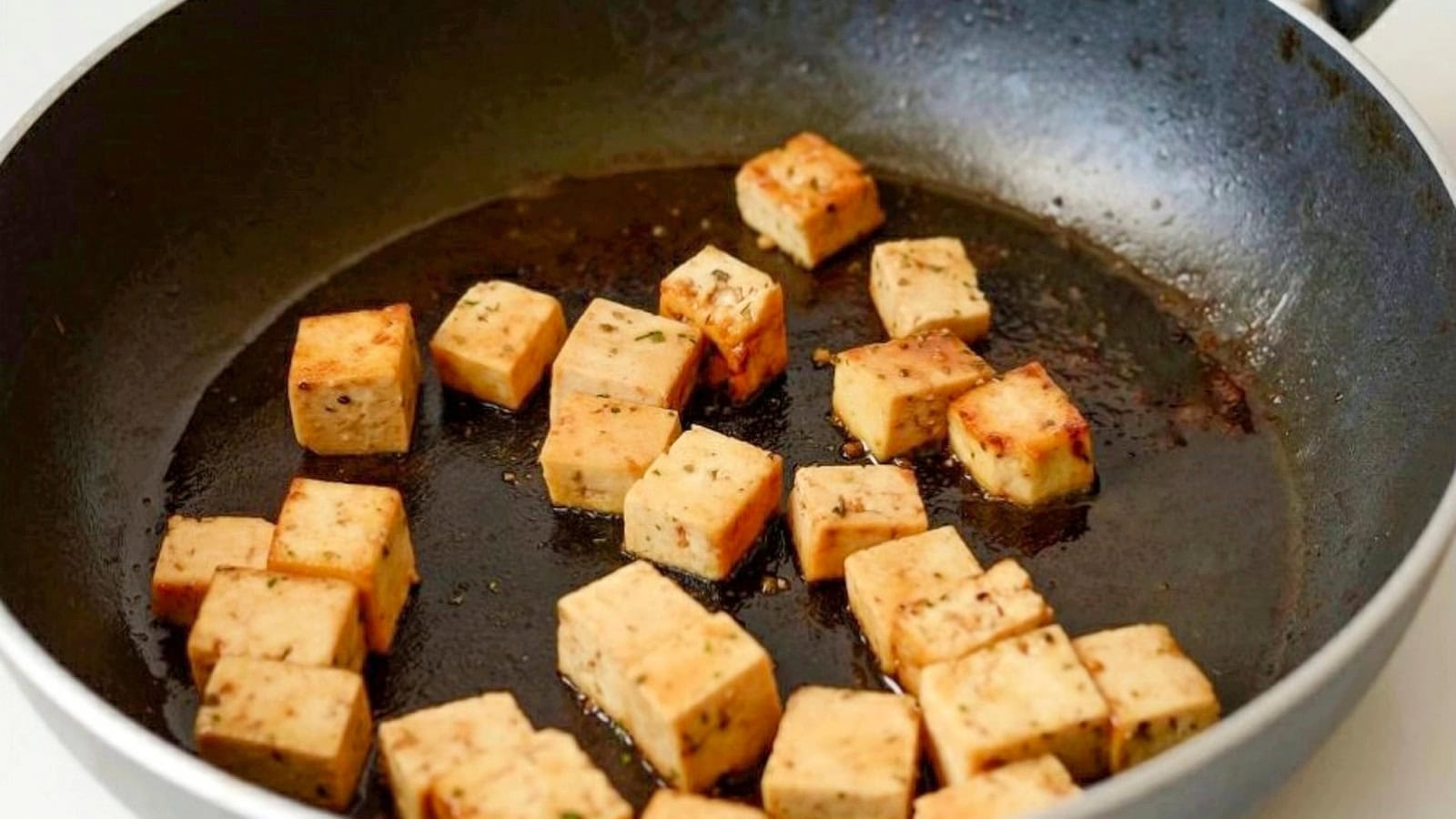 Golden tofu cubes sautéing in a pan.