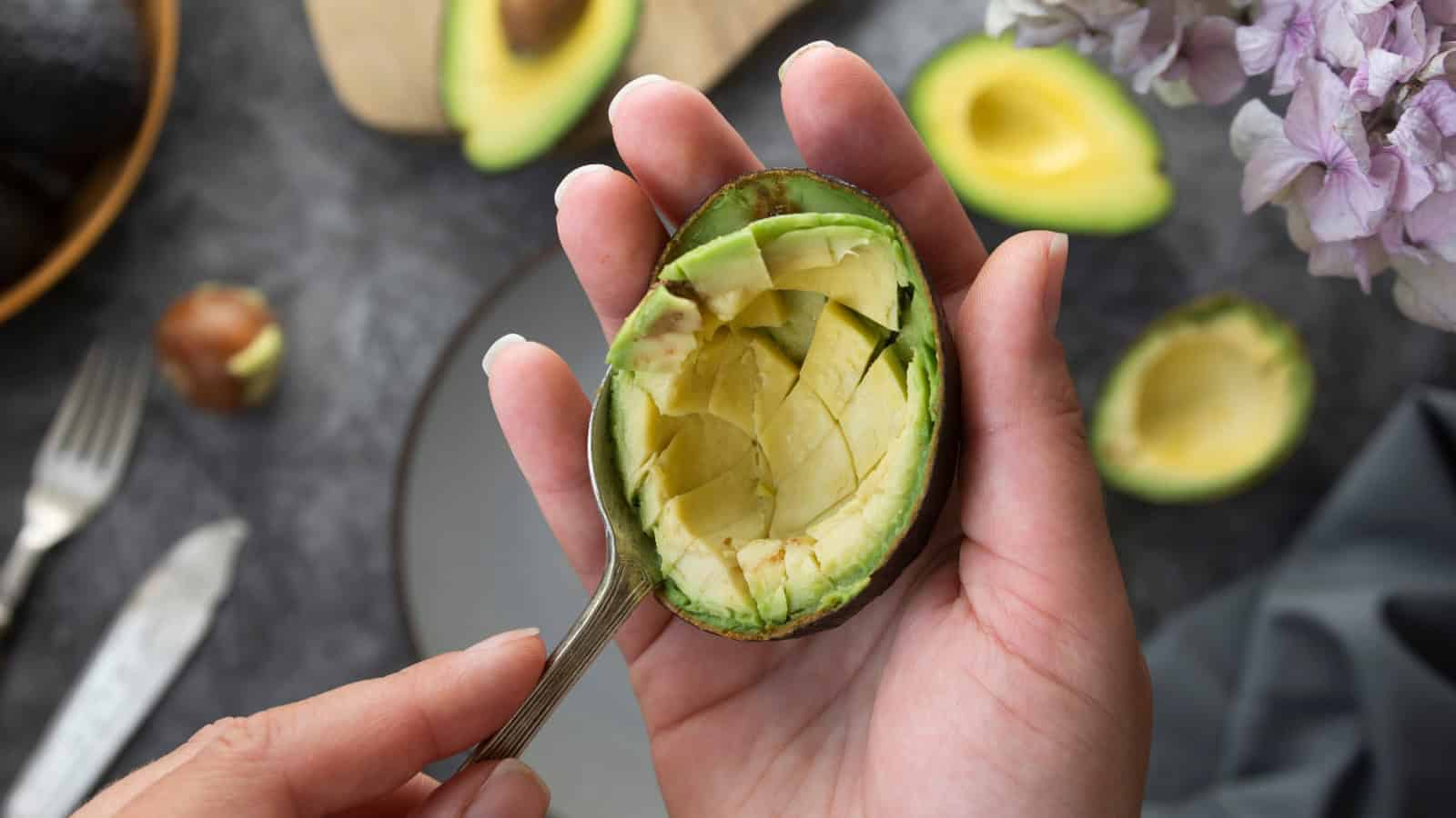 Person scooping avocado flesh from a halved avocado.