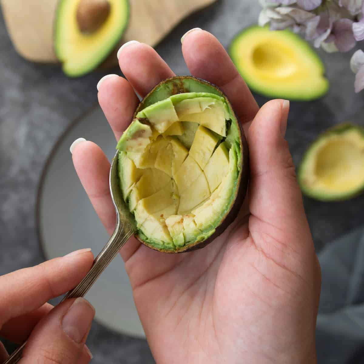 Person scooping the flesh from a halved avocado.